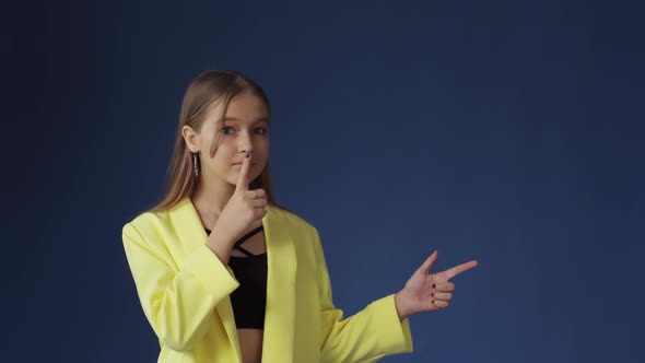 A Beautiful Caucasian Girl on a Dark Blue Background Makes a Gesture of Silence Puts Her Index