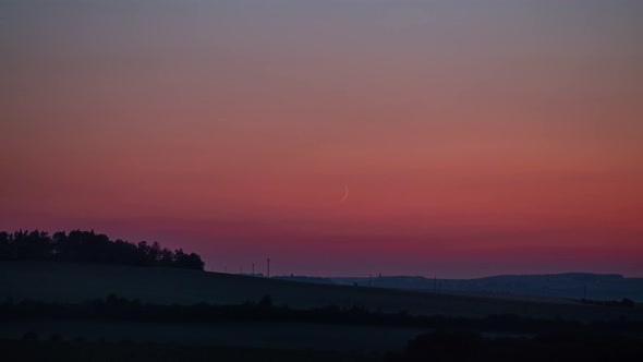 Crescent moon set time lapse with orange sky and short fireworks on the horizon