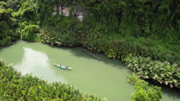 Aerial view of a local boat floating down a green river in Ramang Ramang Sulawesi surrounded by jung