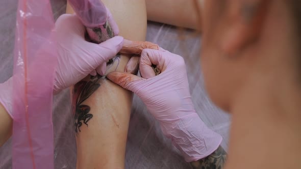 A Woman in Pink Gloves Makes a Tattoo on the Leg of a Young Girl