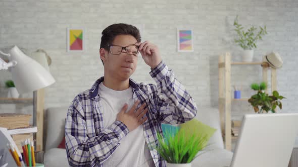 Young Asian Man in a Shirt with a Heartache Sitting at the Laptop