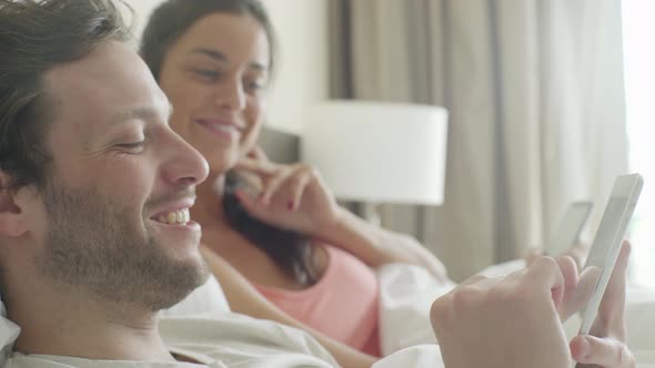 Couple relaxing in bed chatting while using personal wireless devices