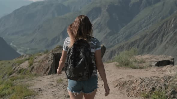 A Female Traveler with a Rucksack Walks Through the Mountains To the Top