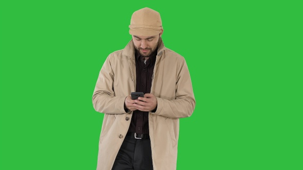 Young handsome man in cloak messaging with phone on a Green