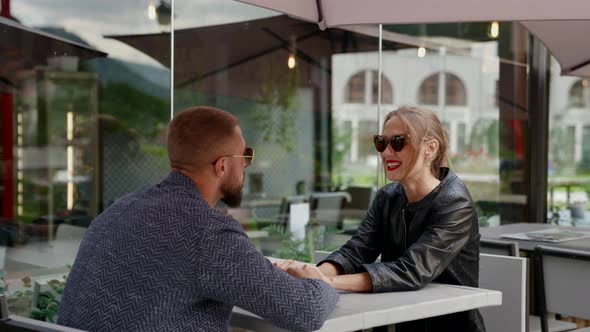 a Couple in Dark Glasses is Sitting at a Cafe Table on the Street