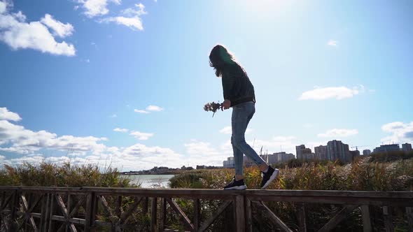 Pretty Nice Girl Walking on Wood Railing with Lake Reeds and Buildings on the Background. Slow