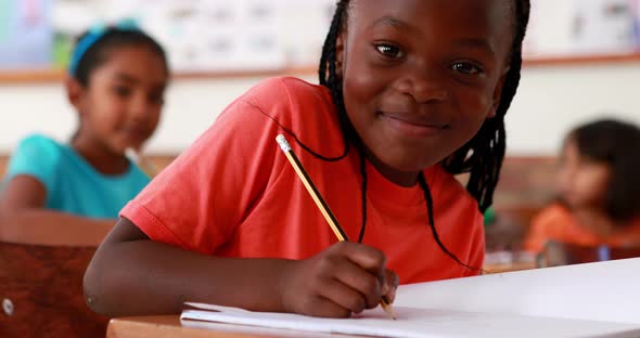 Little gGirl Writing and Smiling at Camera During Class