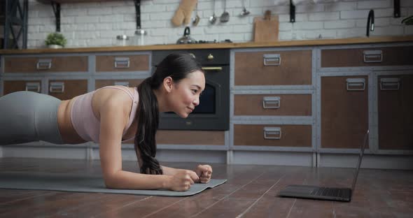 Healthy Asian Yoga Woman Standing in Plank with Online Trainer Using Laptop