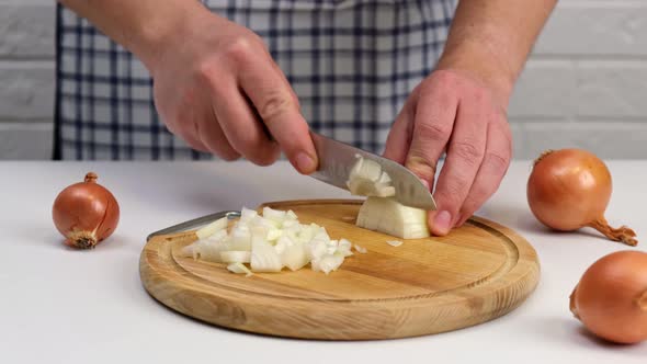 Man's hand slicing onion on a wooden cutting board.