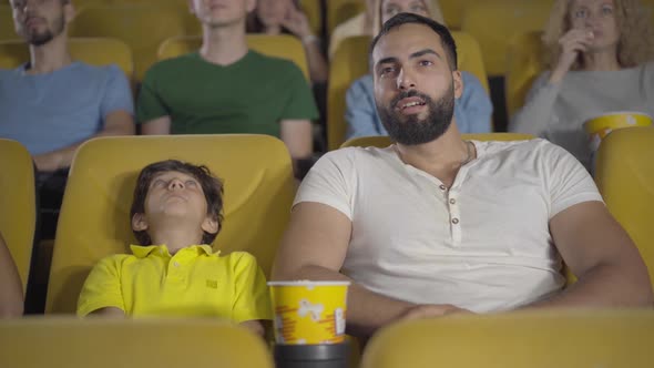 Cheerful Middle Eastern Man and Boy Watching Film in Cinema and Talking. Portrait of Happy Father