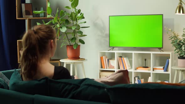 Woman Watching TV with Green Screen in Living Room Back View