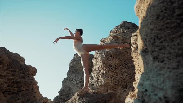 Dancing Ballerina Among Rocks Near Ocean or Sea at Sunrise or Sunset. Portrait of Flexible Woman