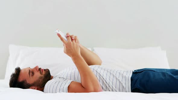 Man using mobile phone on bed in bedroom