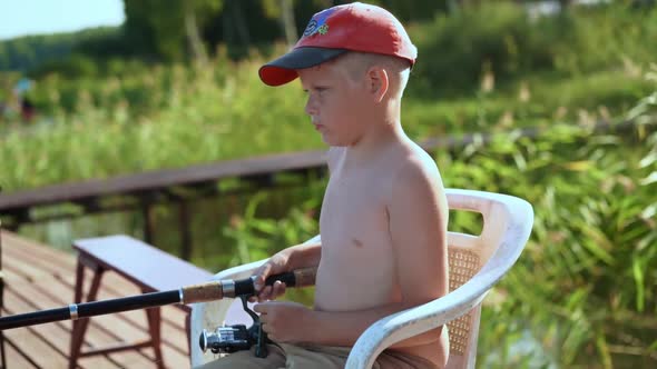 CUTE LITTLE CAUCASIAN BOY SITTING ON PIER FISHING Using Fishing Pole