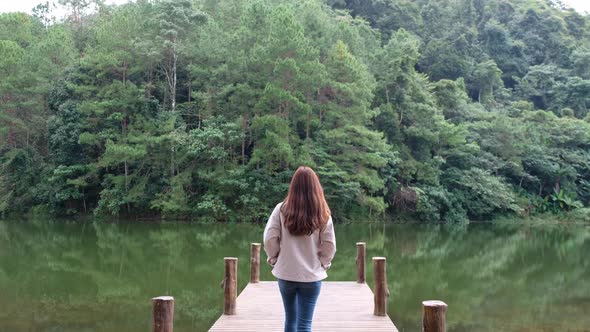 Rear view of a female traveler walking on wooden dock by the lake