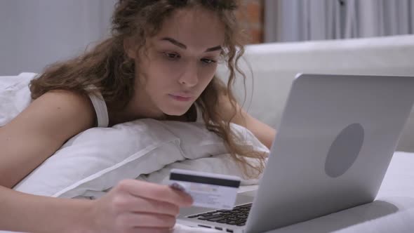 Female in Bed Using Bank Card for Online Payment on Laptop