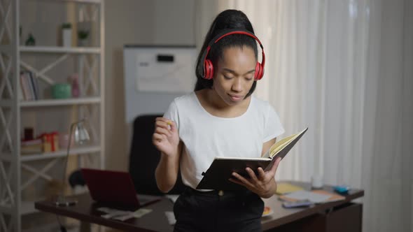 Positive Creative Young African American Woman in Headphones Dancing to Playlist Writing in