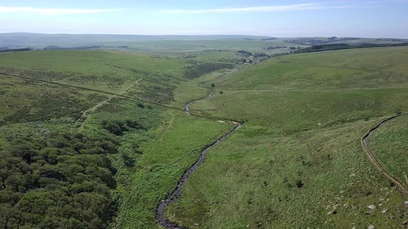 Wide aerial shot tracking forwards and down, with wistmans wood, a river and grassy moorland setting