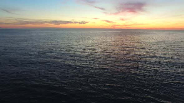 Aerial shot of the sun setting over the ocean horizon.