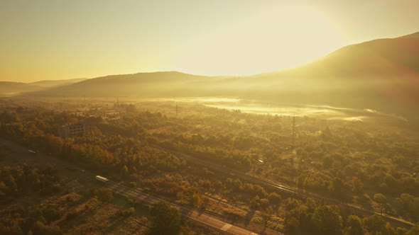 Cinematic Aerial View Fro Drone at Road with Cargo Vehicles and Railways at Sunny Sunrise in