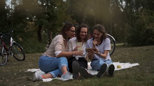 Three Young Women Looking at the Smartphone While Doing Picnic in the Park