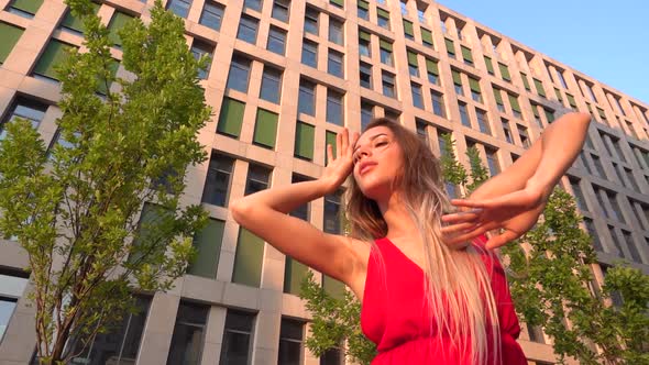 Beautiful Young Girl Dancing on the Street of a Modern Building of a Business Center in the Sunset