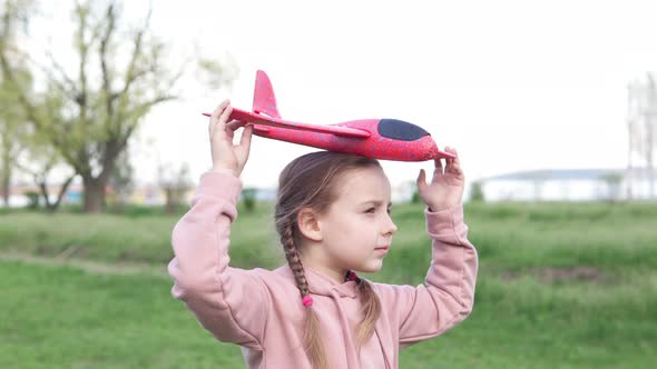 A girl in the park plays with a toy plane, she wants to become an astronaut. Dreamer pilot.