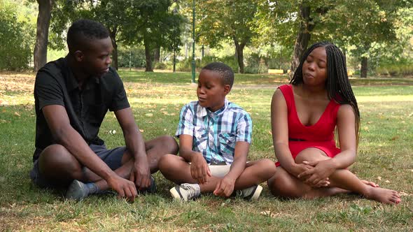 A Young Black Family Sits on Grass in a Park and Talks To Each Other
