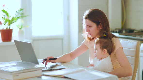 Young Mother Working on Laptop at Home While Her Child Siting on Her Lap