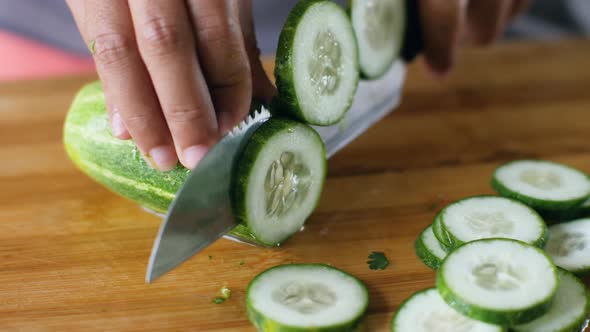 Macro of Slicing a Fresh Cucumber with Kitchen Knife on a Wooden Cutting Board.