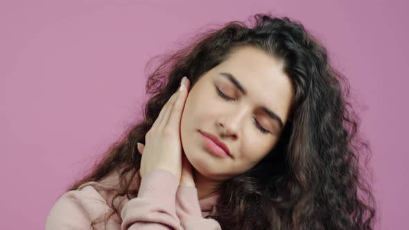 Closeup Portrait of Young Woman Yawning and Rubbing Face on Pink Background