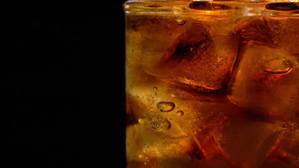 Cola with Ice and Bubbles in Glass Rotate on Black