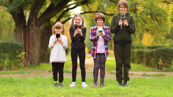 Happy Children Friend Girls Group Walk Together in Summer Park and Playing Internet Game with Mobile