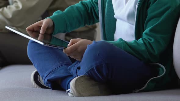 Son Playing Tablet Game Sitting With Father on Sofa in Waiting Room, Addiction