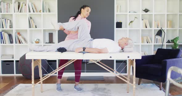 Video of happy biracial female physiotherapist exercising with caucasian senior man