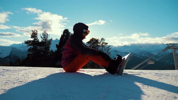 Girl with Snowboard Sitting on Top and Enjoying Mountain Landscape. Sport Woman in Snowy Mountains
