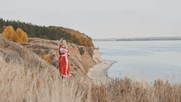 A Woman Warrior in Red Dress Standing on the Mountain Cliff and Wields a Sword