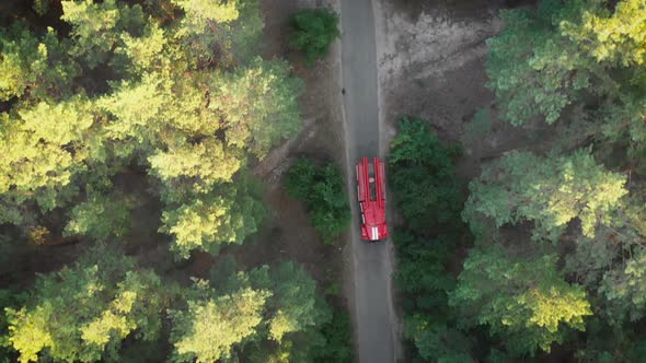 Top View From the Drone To the Red Fire Truck Driving Along the Road in a Pine Forest