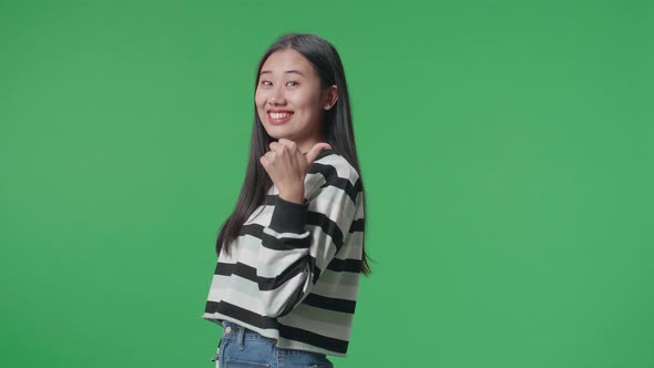 Asian Woman Pointing To The Back Behind By Thumbs Up While Standing On Green Screen