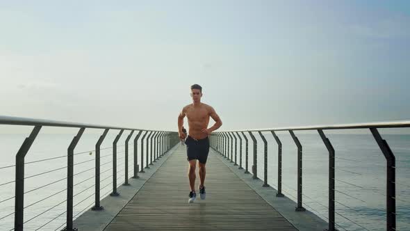 Young attractive athlete running half naked to the camera on a Bridge in the morning from a perspect