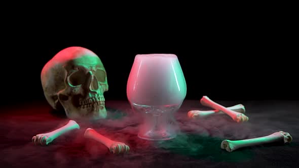 Cognac Glassful with Smoke Near the Skull and Bones on a Black Background. Slow Motion