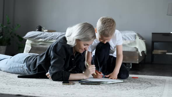 A Young Mother and a Baby Boy Are lying on the Floor, Drawing with Felt-Tip Pens on Paper
