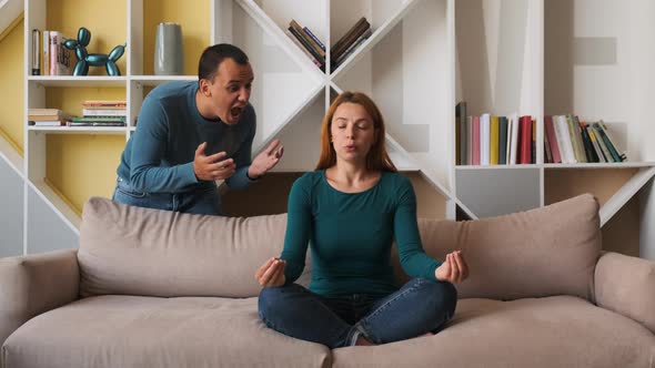 Desperate Girlfriend Meditating Sitting on Sofa While Boyfriend Screams Accusing Her 