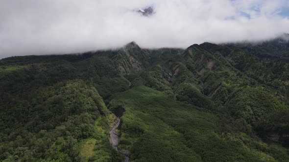 Aerial view of flying in a tropical forest, mountain, and valley in Indonesia.