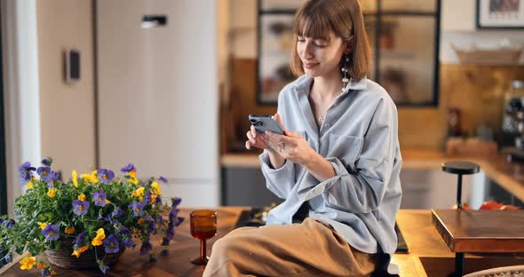 Woman Sits on a Kitchen Top with Phone at Beautiful Home