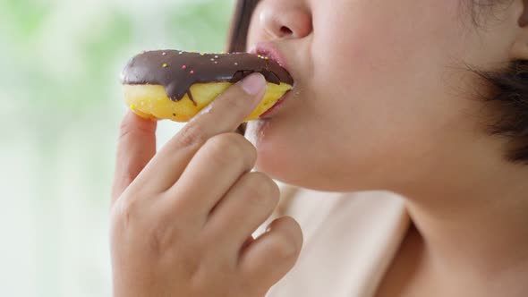 Close up of oversize big women eat unhealthy foods, bite sweet chocolate donut in kitchen at home