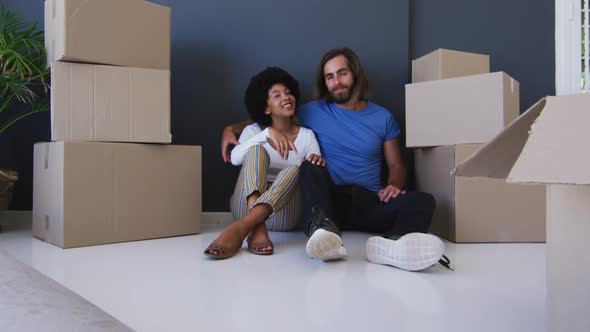 Mixed race couple sitting in between cardboard boxes at new apartment house