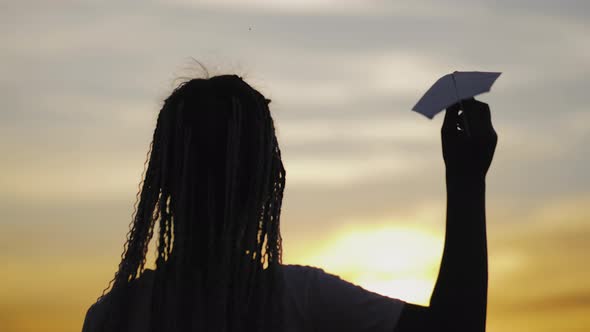 Happy Little Girl Playing with a Paper Airplane Outdoors During Sunset