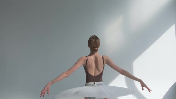 Ballerina on a White Background Standing with Her Back Performs Smooth Movements with Her Hands