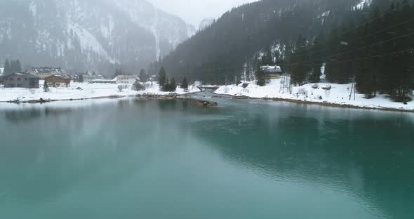 an island with spruces over blue cyan water with stone pier during heavy snow